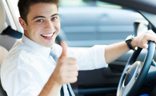 Zadowolony młody chłopak w białej koszuli z krawatem prowadzący samochódz
